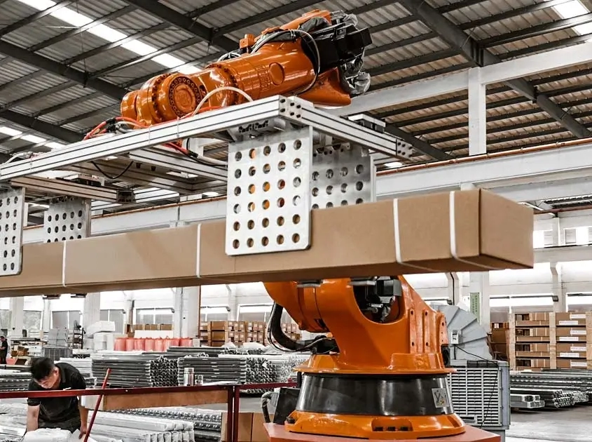 Robotic arm lifting packaged boxes from conveyor in modern pergola factory