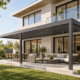Modern aluminum louvered pergola attached to a two-story house, aligned with the home's balcony and exterior architecture.
