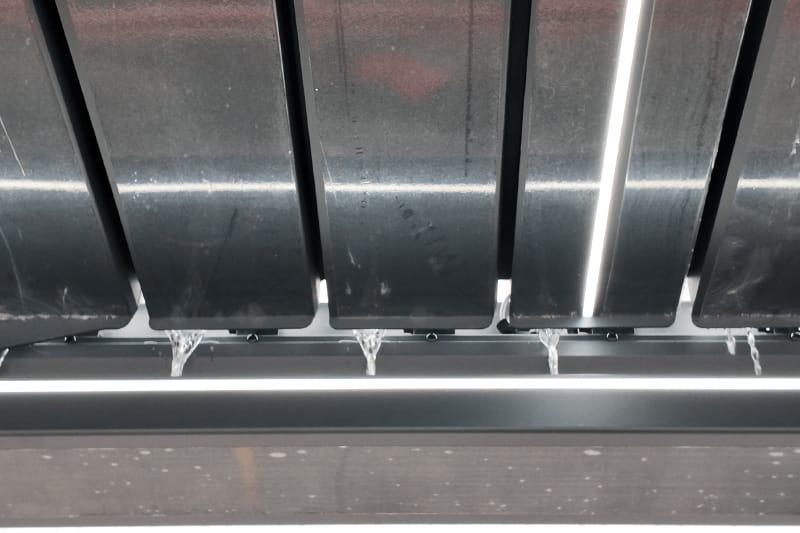 Rainwater flowing from pergola louvers into the integrated beam gutter